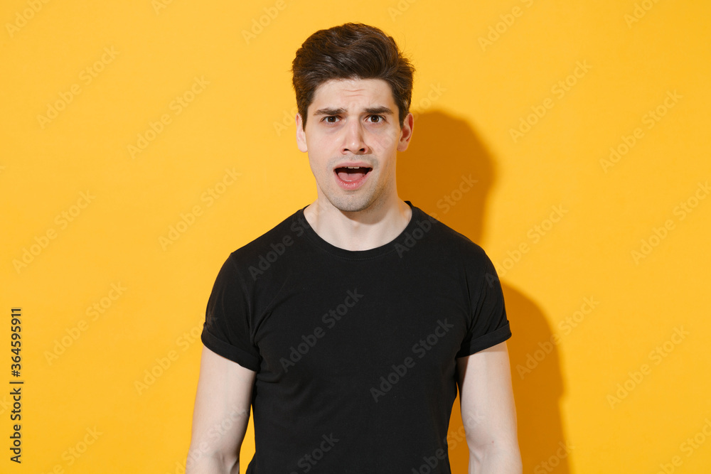 Shocked perplexed young man guy wearing casual black t-shirt posing isolated on yellow background studio portrait. People sincere emotions lifestyle concept. Mock up copy space. Keeping mouth open. Shocked perplexed young man guy wearing casual black t-shirt posing isolated on yellow background studio portrait. People sincere emotions lifestyle concept. Mock up copy space. Keeping mouth open.