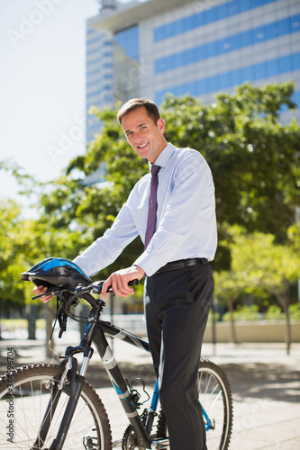 Smiling businessman with bicycle and helmet in urban park