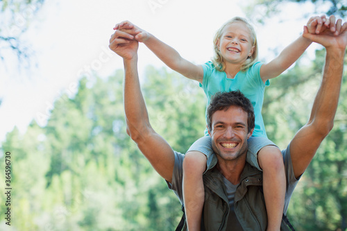 Smiling father carrying daughter on shoulders in woods