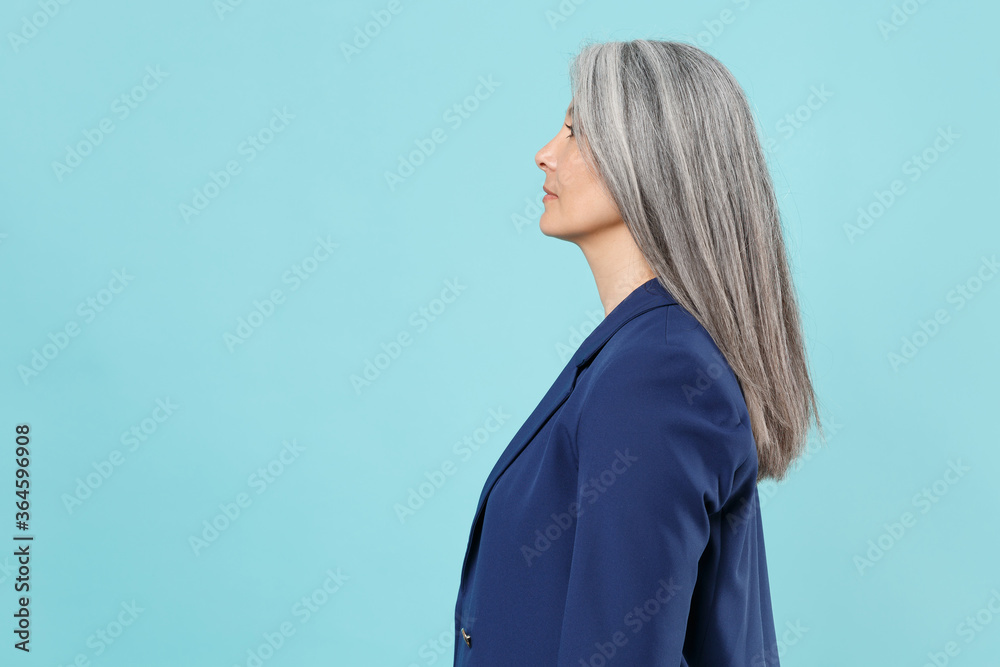 Side view of confident gray-haired business woman in blue suit posing isolated on pastel blue background studio portrait. Achievement career wealth business concept. Mock up copy space. Looking aside.