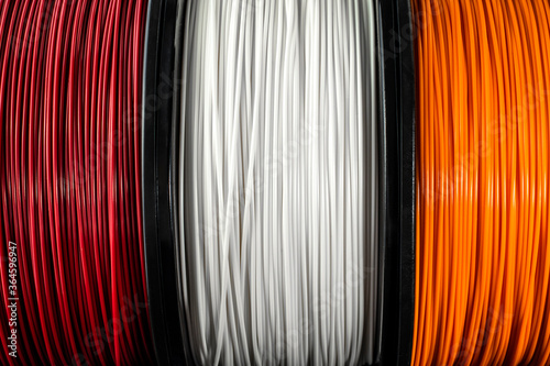 Three coils of filament for 3d printing. Bright thermoplastic of red, white smd orange colors.