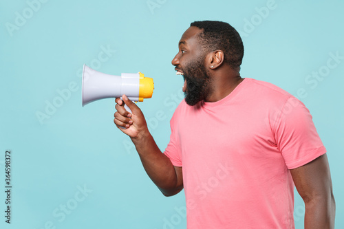 Excited young african american man guy in casual pink t-shirt isolated on blue wall background studio portrait. People lifestyle concept. Mock up copy space. Screaming on megaphone, looking aside.