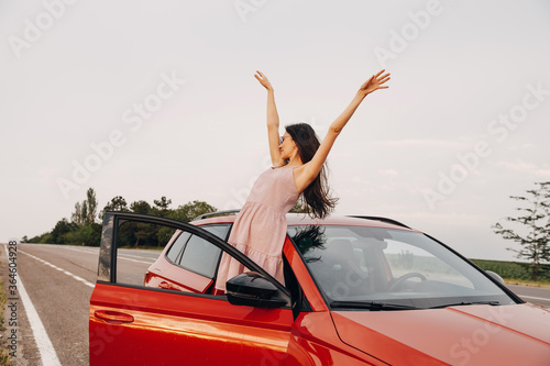 Young woman with hands up in the air out of a car. Summer road trip concept.