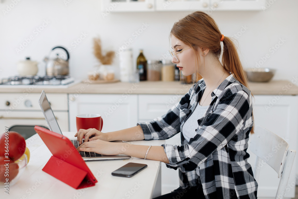 Young woman working in laptop and tablet at home at her kitchen Young woman working in laptop and tablet at home at her kitchen