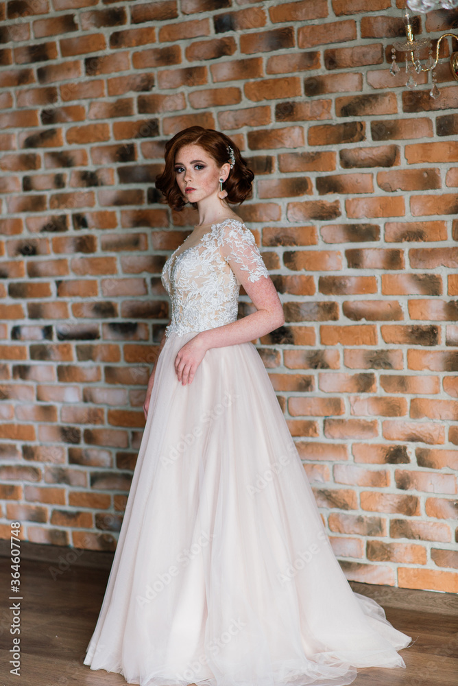 Fototapeta premium Portrait of red haired girl wearing wedding dress against a white studio background.