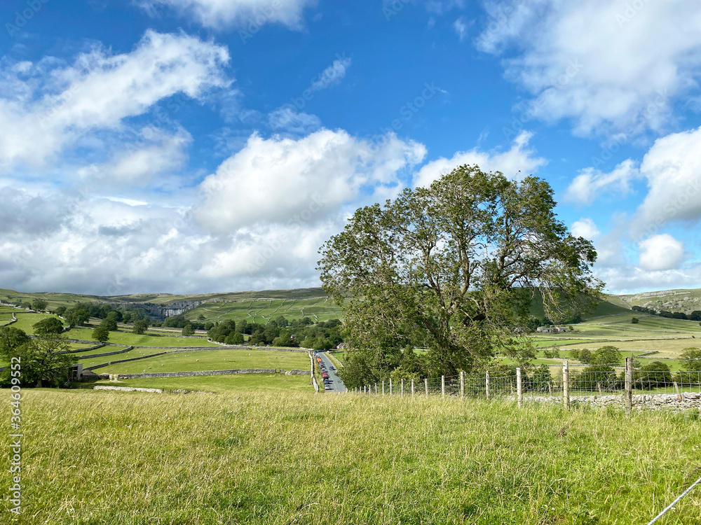 Landscape view, looking toward Gordale Scar, with Malham village nestled amongst trees, past the parked cars. Landscape view, looking toward Gordale Scar, with Malham village nestled amongst trees, past the parked cars.
