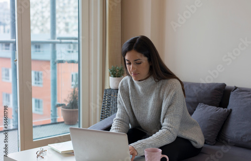 Young woman working on a laptop by the window at home in Birmingham, Uk.