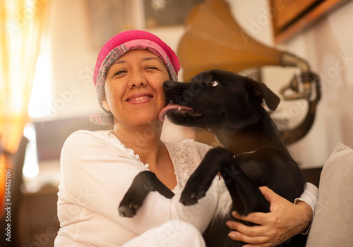 latin woman hugging her pet, woman with pink scarf on her head due to breast cancer
