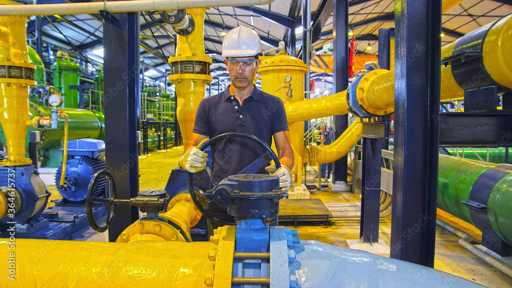 worker in industrial installation turning big wheel on pipeline
