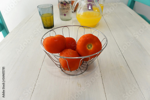 Fototapeta Naklejka Na Ścianę i Meble -   tomatoes inside a bowl on top of a white table with a few glasses and bottles behind      