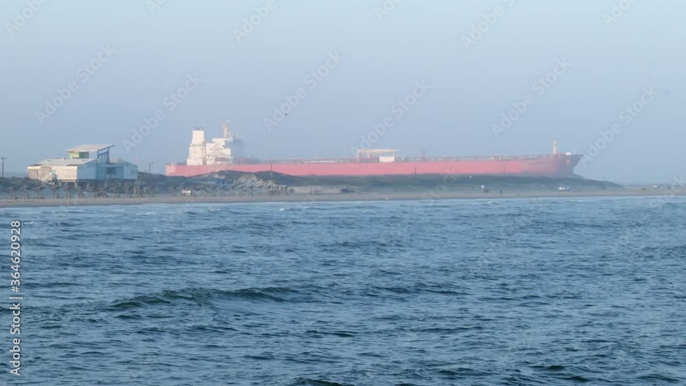 Ocean sailing oil tanker ship approaches the waters of the Gulf of Mexico in Port Aransas, Texas on a hazy evening, with waves and beach and copy space, in slow motion clip. Ocean sailing oil tanker ship approaches the waters of the Gulf of Mexico in Port Aransas, Texas on a hazy evening, with waves and beach and copy space, in slow motion clip.