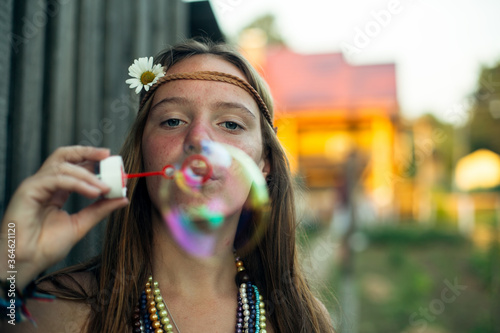 Young cute hippie girl, in the village, blows soap bubbles.