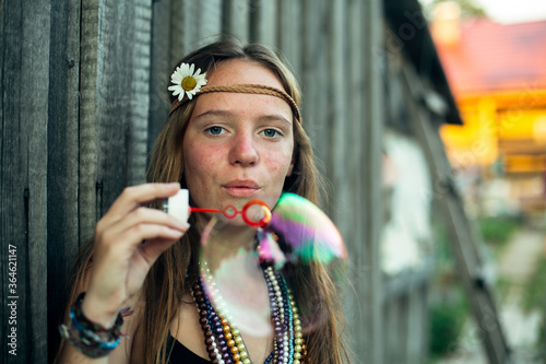 A young hippie girl, in the village, blows soap bubbles.