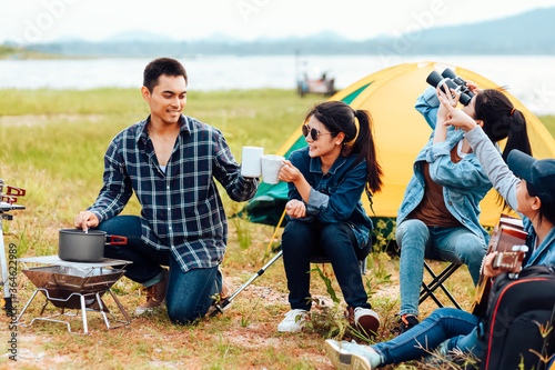 A group of friends camping happily near the lake on a holiday. A woman plays the guitar for a friend to listen. © Charnchai saeheng