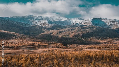 The beautiful autumn landscape on Senja island. Light wispy clouds passing above the mountains with snow-covered peaks and a vast valley. Forest is painted orange, red, yellow, and rust. photo