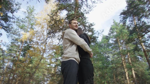 Handsome man soothingly embosoms attractive female. Couple standing in brightly lit autumn forest. Low angle 4K 360 degree tracking arc shot. photo