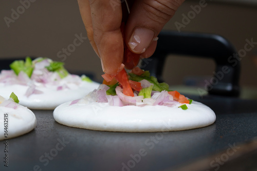 adding sliced tomatoes and capsicum on round utappa south indian dish with fingers