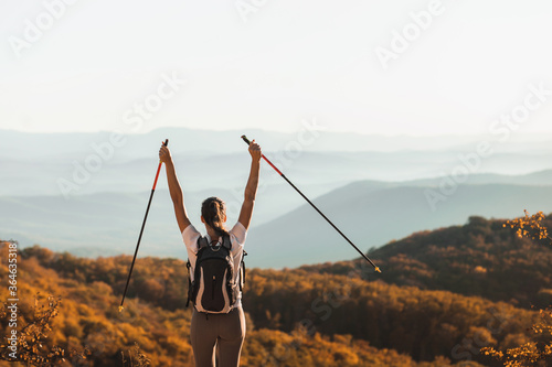 Woman happy to hike top of mountain and hold trekking poles. Nordic walking outdoors, view from behind. Travel lifestyle. Success goal achievement.