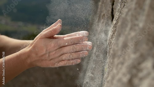 SLOW MOTION, CLOSE UP, DOF: Unrecognizable climber claps her hands to get rid of excess magnesium before continuing her ascent. Woman top rope climbing chalks up her hands midway during her climb photo