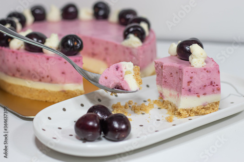 Cherry cheesecake with tea spoon and piece of cake on white plate.