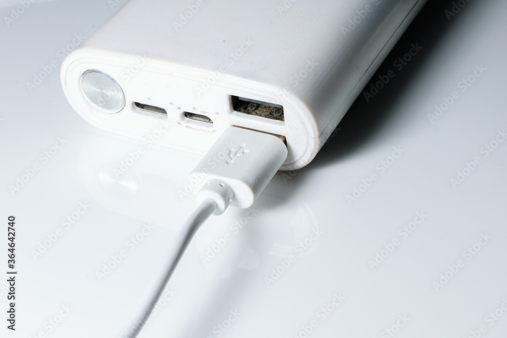 A white power bank with USB ports and power button. A cable is attached to one of its ports A white power bank with USB ports and power button. A cable is attached to one of its ports