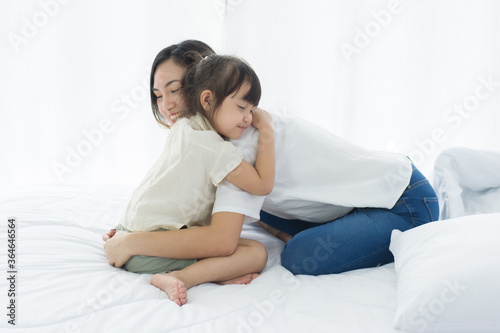 Lovely Asian mother and little daughter hug together, smile and feeling happy on the bed in a cozy house, family concept.
