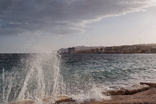 late afternoon sun lights up breaking wave on Hananya Beach on the Gulf of Eilat with low clouds above and the resort city of eilat in the background