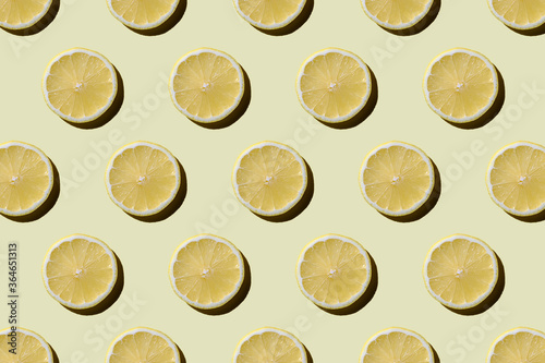 modern pattern of round lemon slices with a hard shadow on a pastel yellow background. Fashionable summer concept