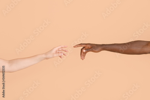 Hands of Caucasian woman and African-American man reaching out to each other on color background. Racism concept photo