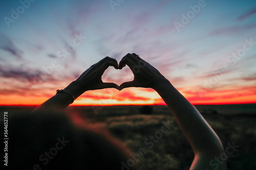Silhouette hand in heart shape with sunrise on the sky background. love concept. Love sign. Woman making heart with her hands at sunset.