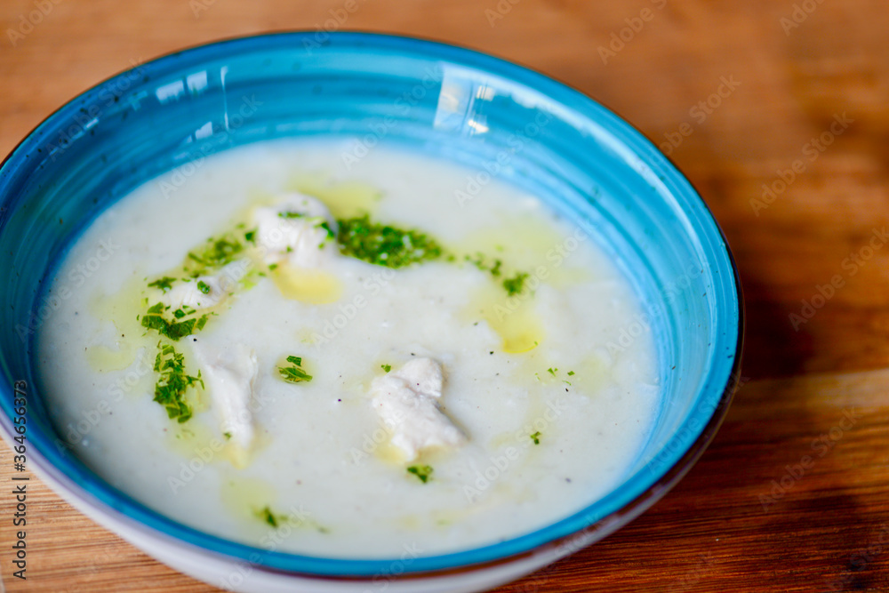 Serving of cream soup with meat and gresh greenery. Served in a blue bowl over rustic wooden background.