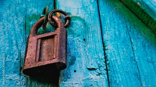 Old lock vintage door colorful photo close up. Old wooden door gate closed with metal chain & rusty iron lock. Close turquoise pastel front door with padlock key of old farmhouse. Safe lock protection