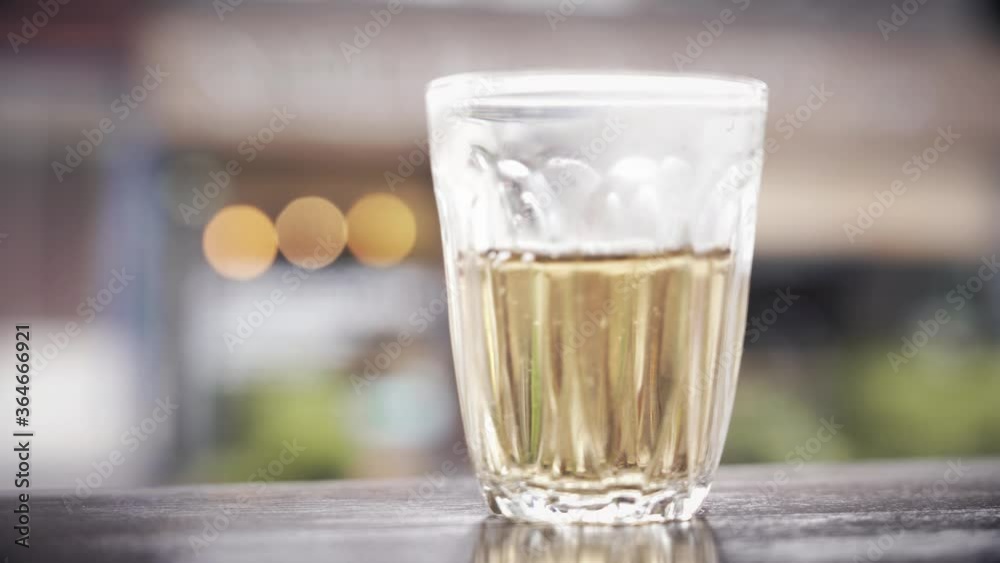 Close-up in a traditional tea glass cup standing on a wooden table in a street cafe pour hot tea. Male hand takes a glass. Traffic in the background. Close-up in a traditional tea glass cup standing on a wooden table in a street cafe pour hot tea. Male hand takes a glass. Traffic in the background.