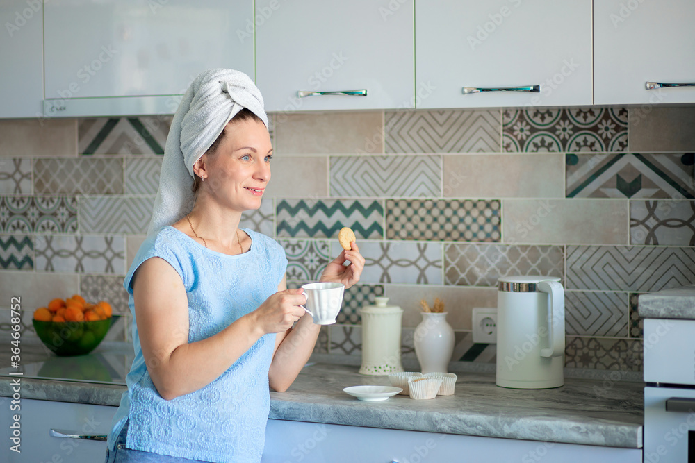 Happy Girl with a towel on her head sutra drinks coffee with cookies for breakfast in his own kitchen at home Happy Girl with a towel on her head sutra drinks coffee with cookies for breakfast in his own kitchen at home