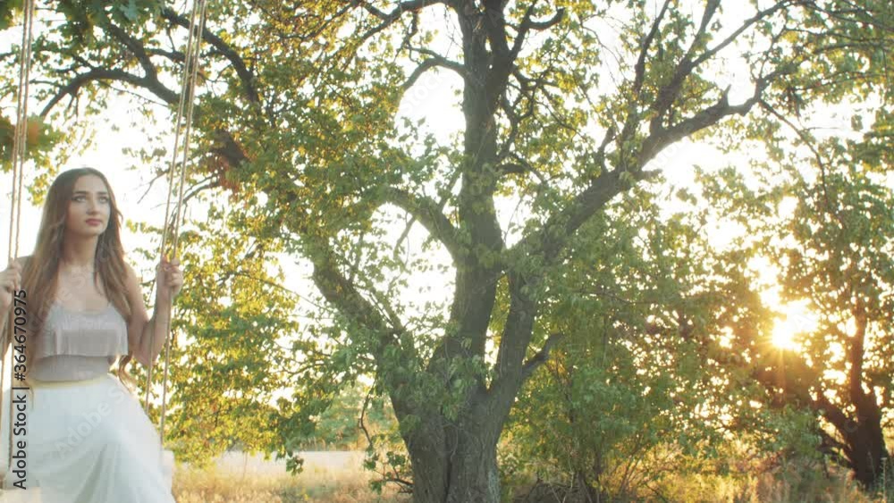 young happy woman sitting and swaying rope swing on oak tree. Female mood, romance, girl have fun in summer at sunset, concept healthy lifestyle young happy woman sitting and swaying rope swing on oak tree. Female mood, romance, girl have fun in summer at sunset, concept healthy lifestyle