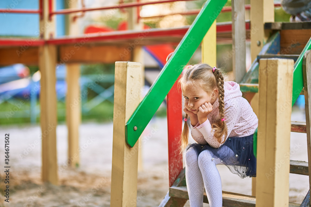 One little baby girl sits on the steps of a playhouse on the playground and holds her head with her hands and thinks One little baby girl sits on the steps of a playhouse on the playground and holds her head with her hands and thinks
