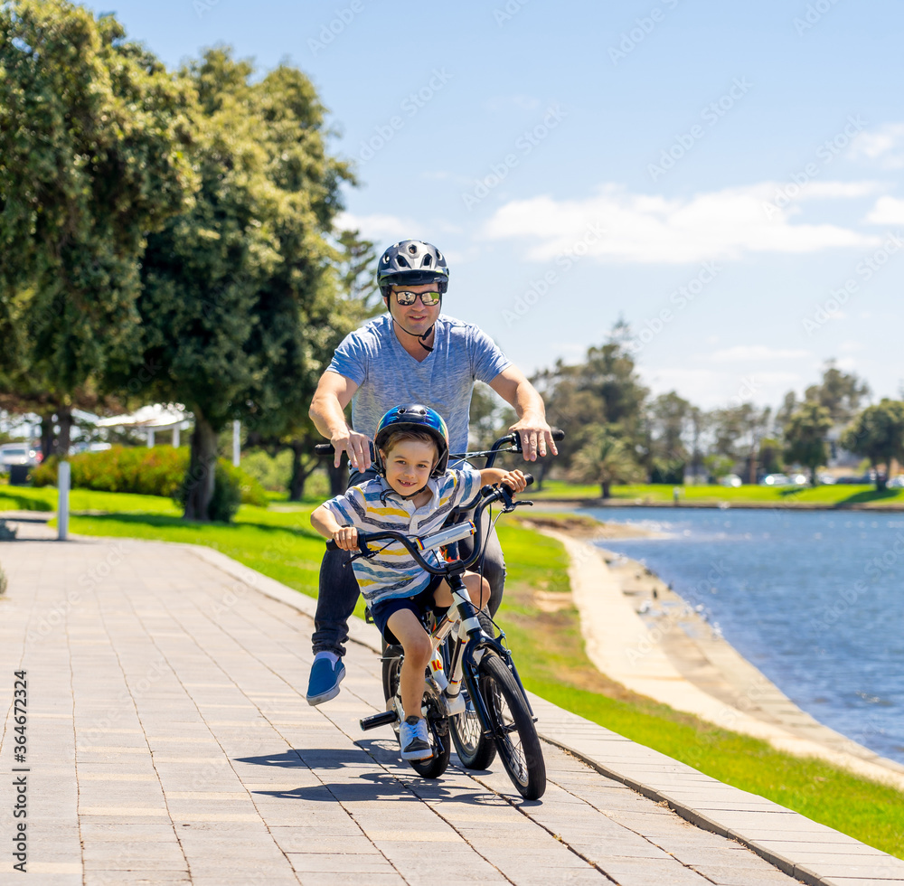 Obraz premium Father and son riding their bikes having fun together in the park by the lake