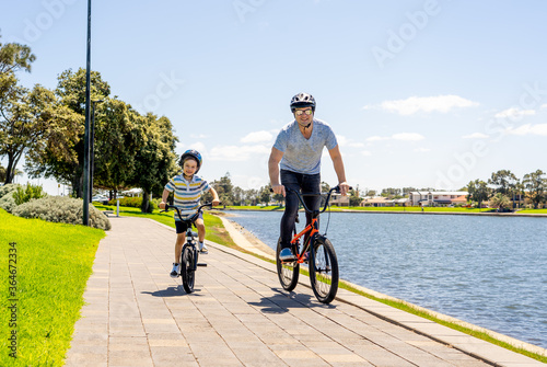 Fototapeta Naklejka Na Ścianę i Meble -  Father and son riding their bikes having fun together in the park by the lake