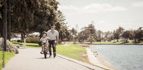 Father teaching his son to ride a bike and having fun together at the park