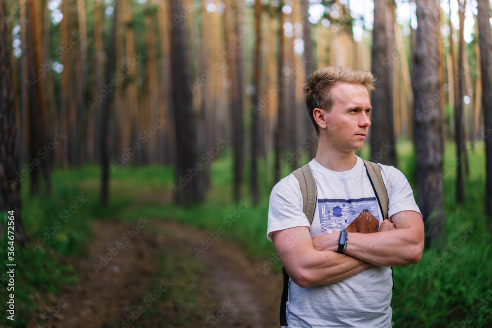A young man with a backpack stands alone in a pine forest with a natural background, the concept of tourism and recreation, a place for text, copy space A young man with a backpack stands alone in a pine forest with a natural background, the concept of tourism and recreation, a place for text, copy space