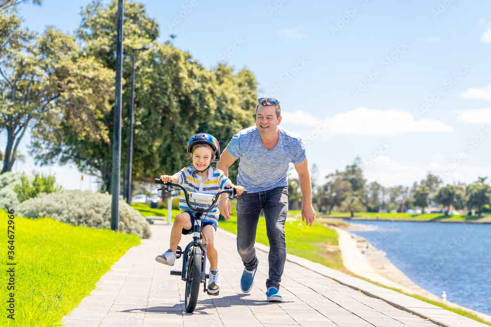 Fototapeta premium Father teaching his son to ride a bike and having fun together at the park