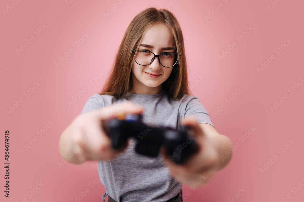 Portrait of cute young girl in eyelasses using joystick for playing video games in studio. Isolated over pink background. Concept of emotions, technology and competition. Portrait of cute young girl in eyelasses using joystick for playing video games in studio. Isolated over pink background. Concept of emotions, technology and competition.
