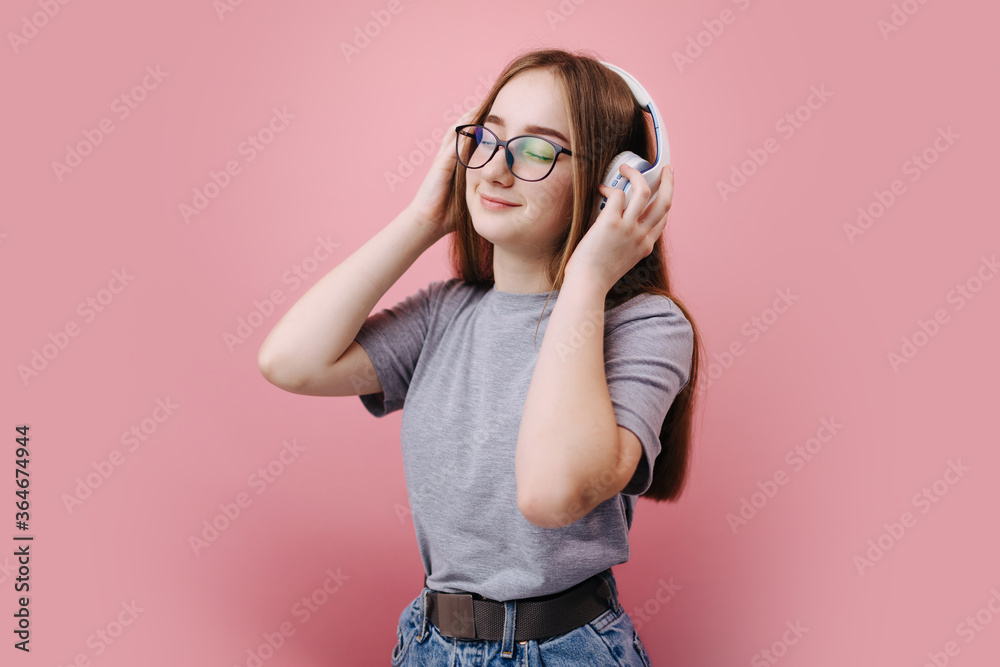 Relaxed young woman with blond hair with closed eyes enjoying favorite music in wireless headphones while standing over pink background. Concept of positive emotion. Relaxed young woman with blond hair with closed eyes enjoying favorite music in wireless headphones while standing over pink background. Concept of positive emotion.