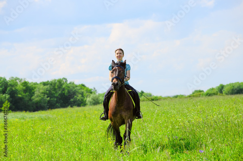 The Caucasian horsewoman is riding on the grass on the summer day.