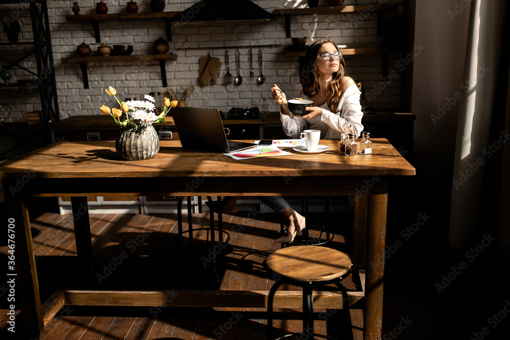 Beautiful young woman have breakfast while working on laptop at the kitchen 