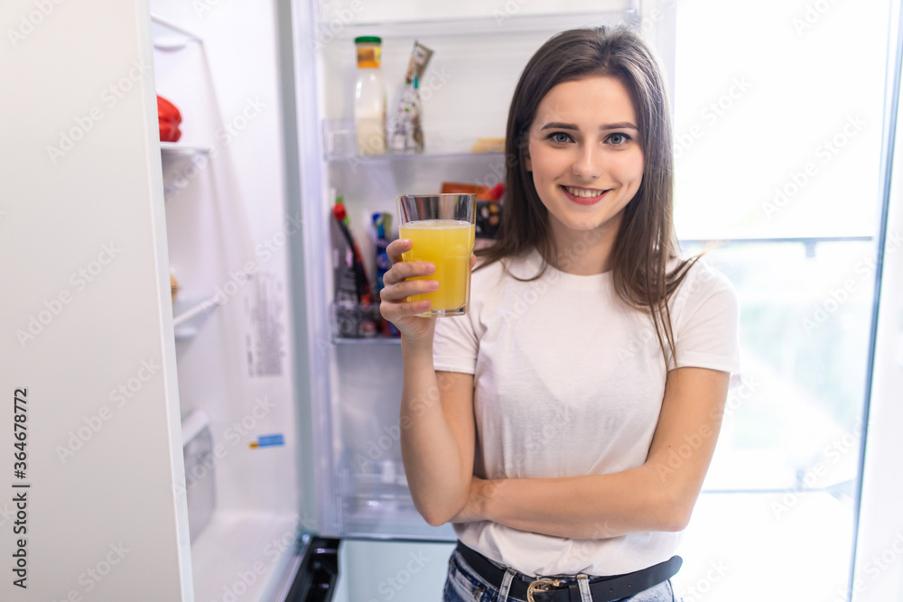 Young woman taking juice out of refrigerator in kitchen Young woman taking juice out of refrigerator in kitchen