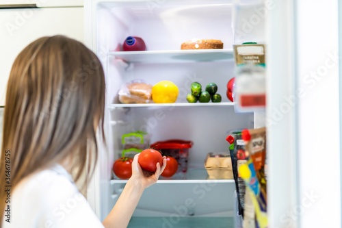 Young woman taking fresh healthy tomato vegetables from refrigerator, view from fridge