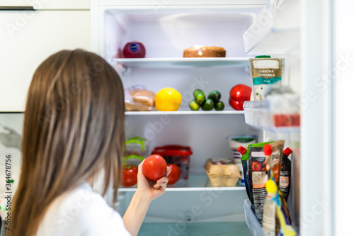 Young woman taking fresh healthy tomato vegetables from refrigerator, view from fridge
