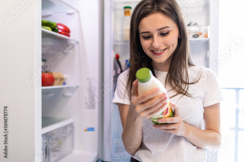 Young woman takes the milk from the open refrigerator