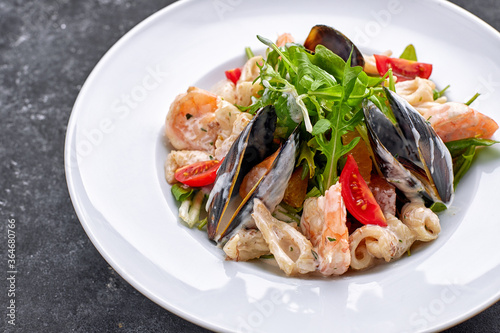Seafood salad with mussels, squid, shrimp, on a round white plate, on a gray background